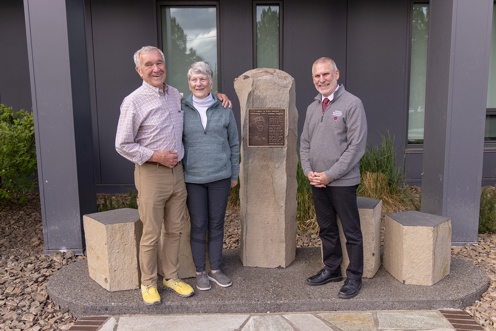Three people stand in front of a memorial made of carved stone